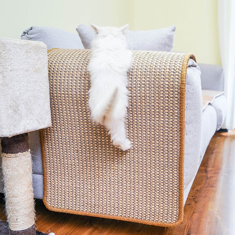 White cat using a natural sisal scratching mat on a sofa